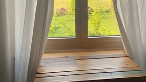 Eine hölzerne Bank an einem Fenster mit weißen Vorhängen, mit Blick auf eine grüne Landschaft.