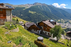 Uma aldeia de montanha com casas de madeira tradicionais, um edifício de pedra e vista para as montanhas circundantes.