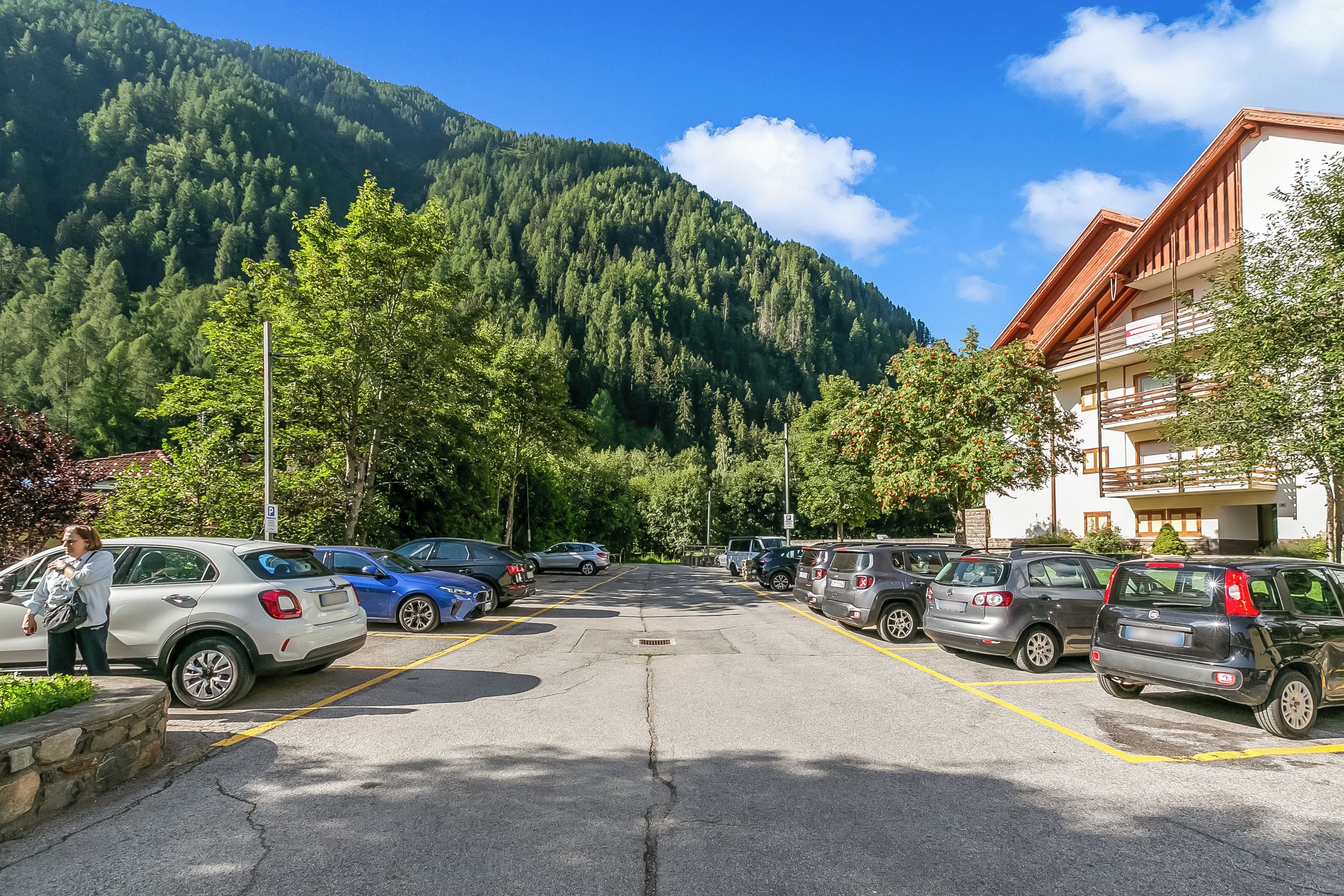 Un parcheggio con auto, un edificio con un balcone e una montagna sullo sfondo.