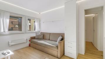 Quarto moderno e bem iluminado, com sofá bege, uma pequena mesa com calculadora e um radiador.