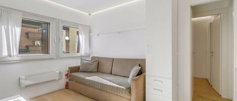 Une pièce moderne et bien éclairée, avec un canapé beige, une petite table sur laquelle se trouve une calculatrice et un radiateur.