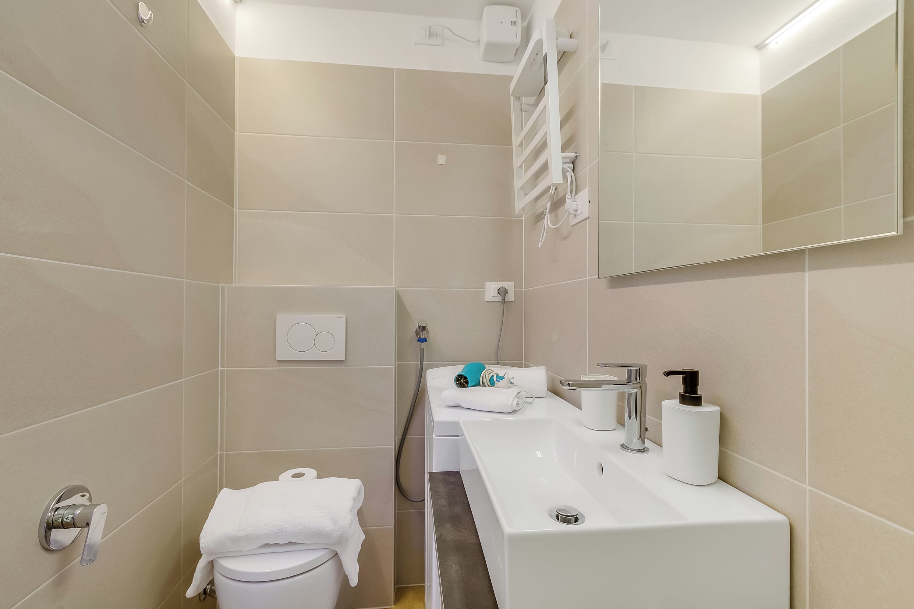 Een moderne badkamer met een witte wastafel, een spiegel, een handdoekhouder en een toilet.