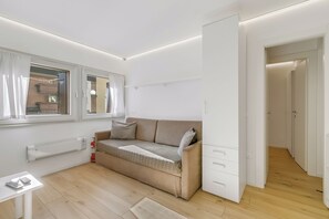 Una habitación moderna y luminosa con un sofá color beige, una mesita con una calculadora y un radiador.