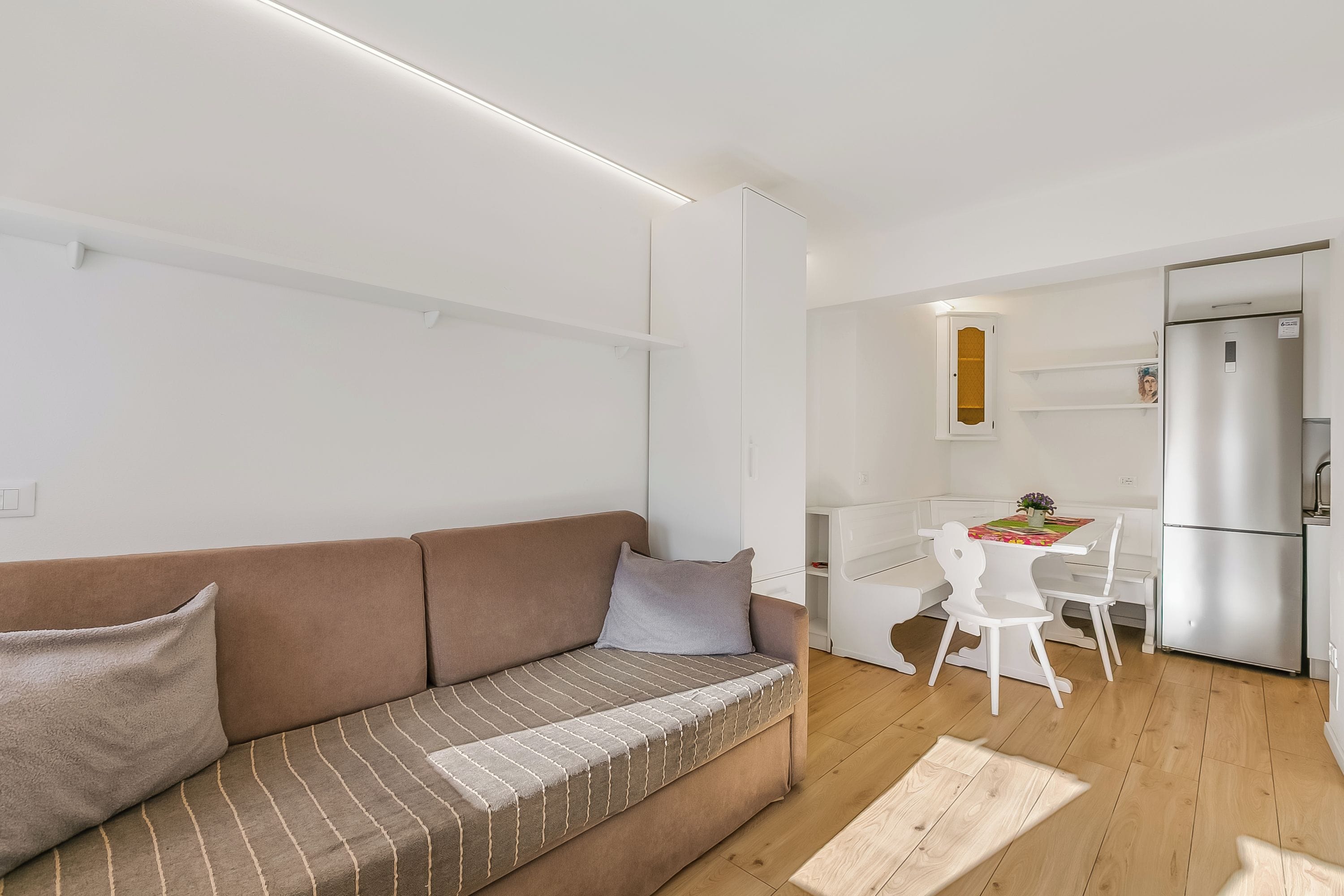 Un salon moderne avec un canapé marron, une table à manger avec des chaises et un coin cuisine équipé d’un réfrigérateur.