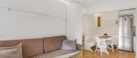 Een moderne woonkamer met een bruine bank, een eettafel met stoelen en een keuken met een koelkast.
