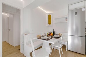 Una cocina moderna con armarios blancos, un refrigerador empotrado y una mesa de comedor para cuatro.