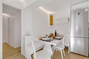 Cozinha moderna com armários brancos, geladeira embutida e mesa de jantar para quatro pessoas.