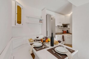 A modern kitchen with white cabinetry, a built-in microwave, and a dining area set with plates, glasses, and a bottle. - Ski In-ski Out Apartment in Peio Val di Sole (Pejo)