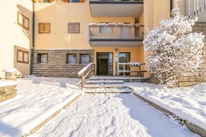 A snow-covered entrance with a stone staircase leading to a building with multiple windows and balconies. - Ski In-ski Out Apartment in Peio Val di Sole (Pejo)