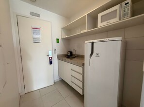 Una cocina compacta con un refrigerador blanco, un microondas y una tetera sobre la encimera.
