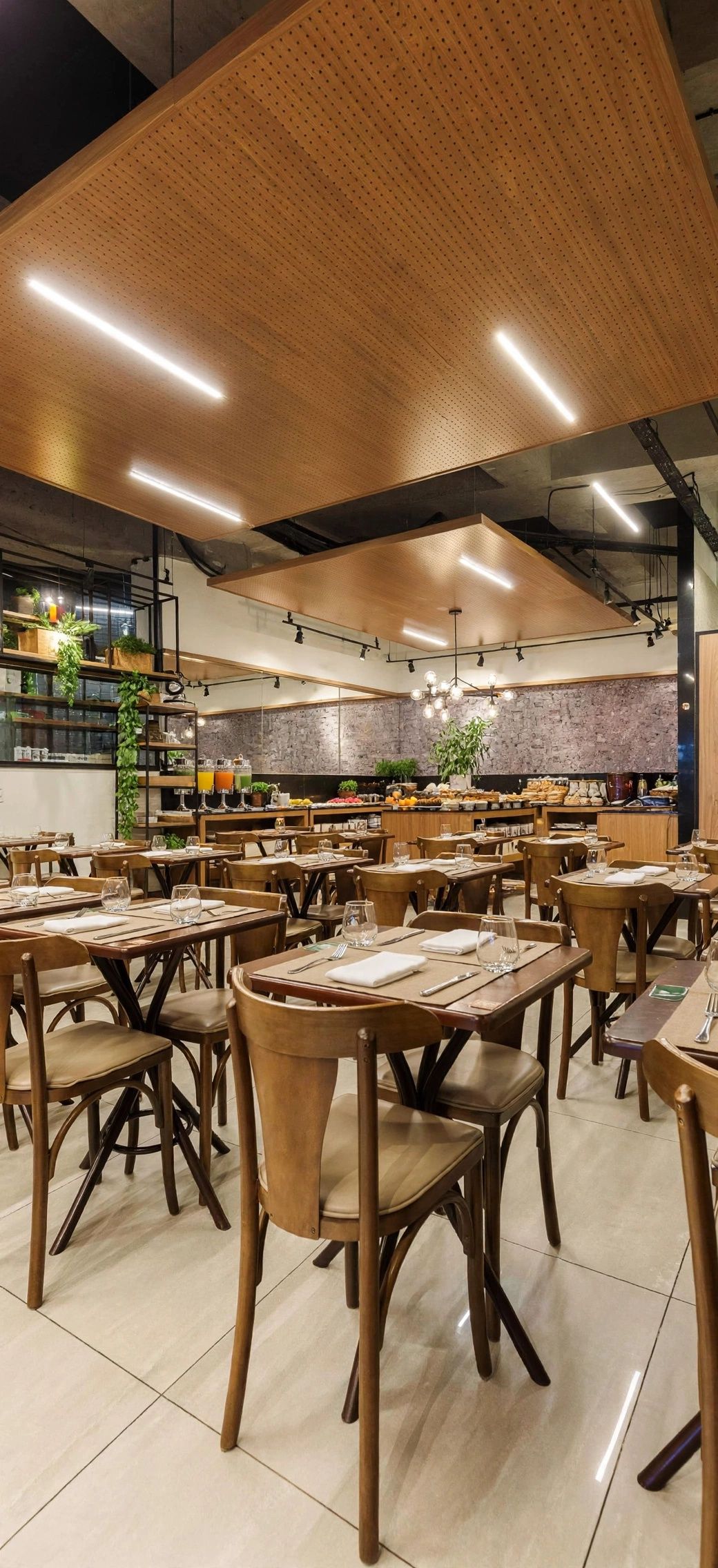 Un restaurante espacioso con varias mesas y sillas, un techo alto con paneles de madera y un área de cocina visible al fondo.
