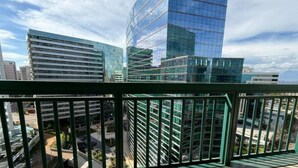 Un edificio alto con fachada de vidrio moderna, barandilla de metal verde y cielo despejado.