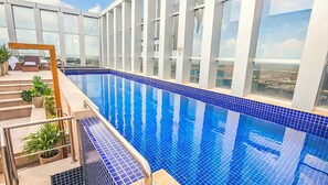 Ein moderner, überdachter Schwimmbereich mit klaren, blauen Kacheln, umgeben von einer Glaswand und einer Treppe, die zu einer erhöhten Ebene führt.