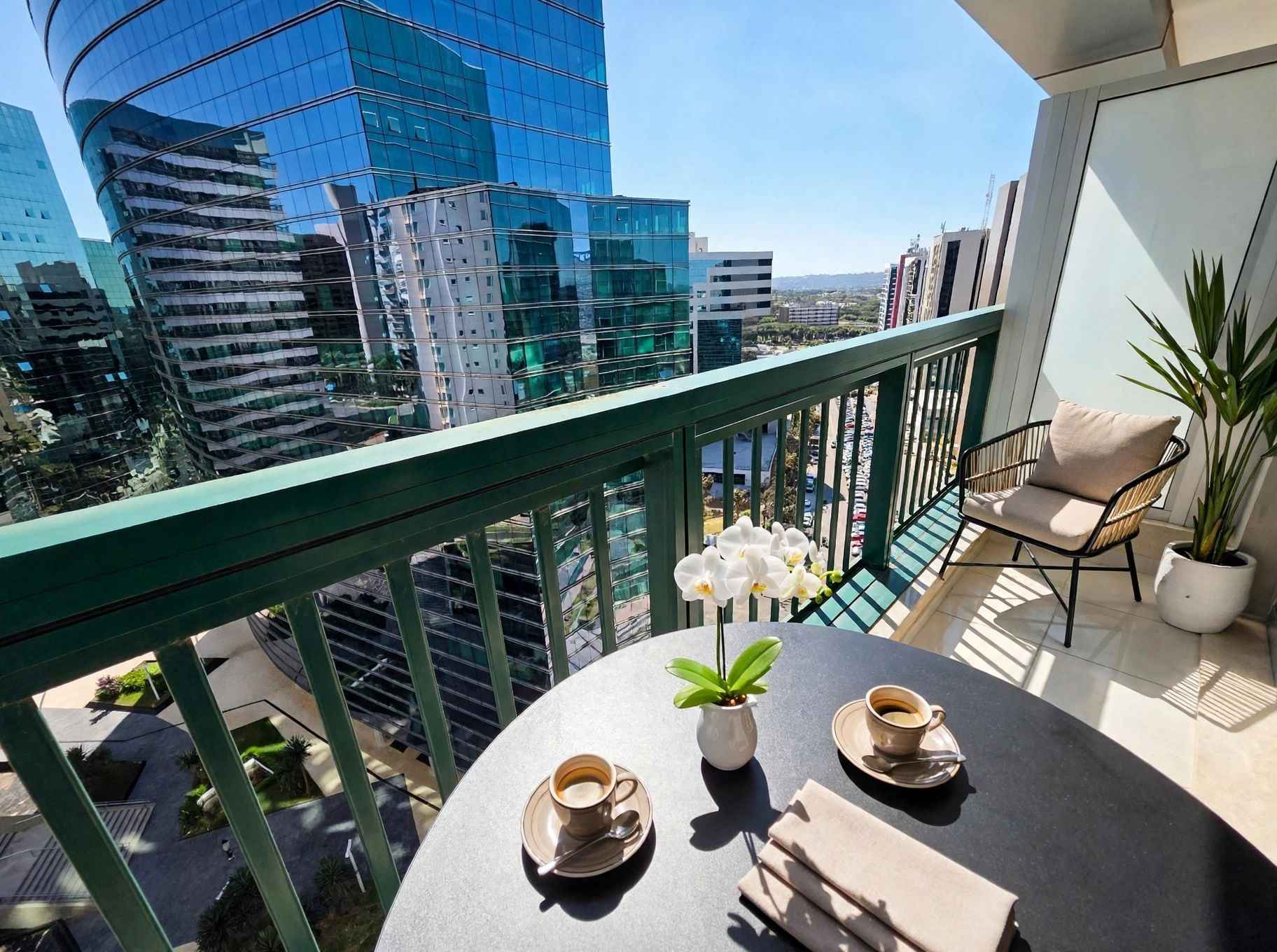 Un balcón con una mesa para dos, una planta en maceta y vistas a edificios modernos.