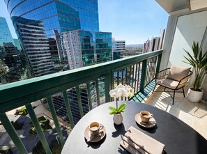 Un balcó amb una taula preparada per a dues persones, una planta en test i vista d'edificis moderns.