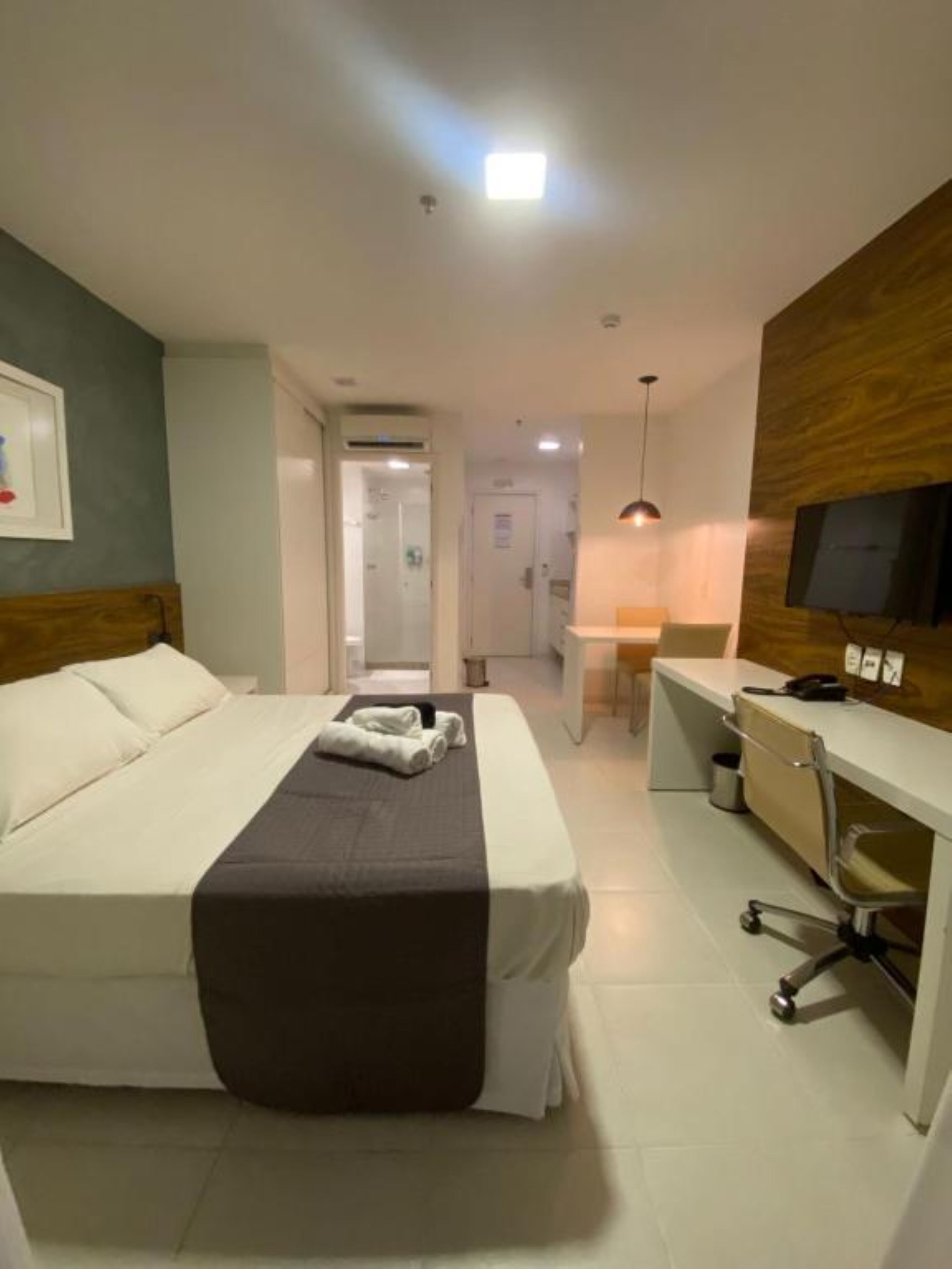 Ein Hotelzimmer mit Bett, Schreibtisch, Stuhl, Fernseher und einem im Hintergrund sichtbaren Badezimmer.