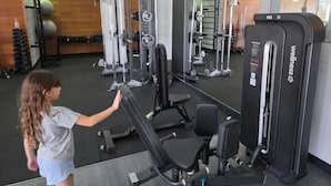 Un gimnasio con diferentes máquinas de ejercicio, una banca y pesas.