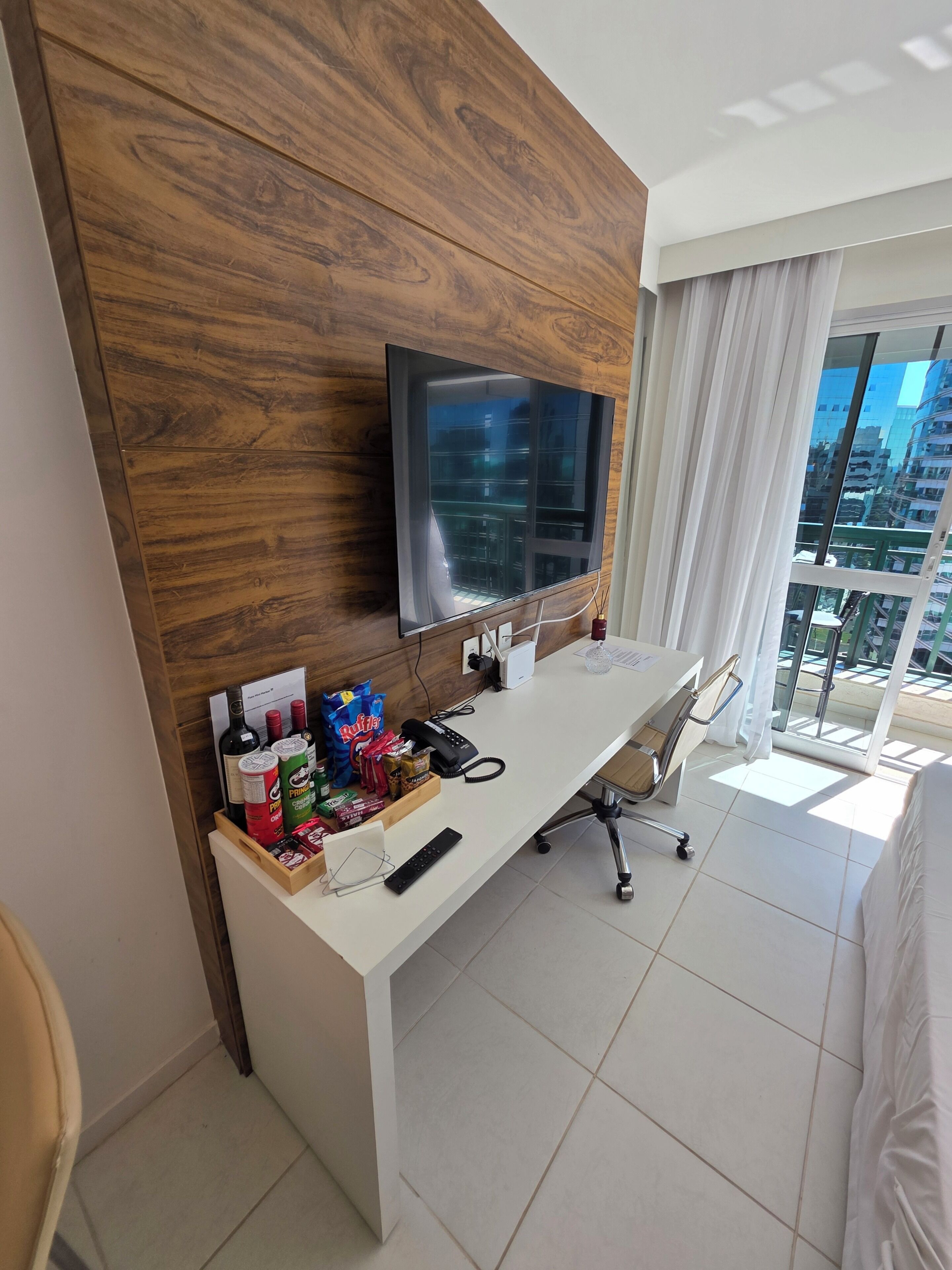 Een hotelkamer met een houten accentmuur, een flatscreen-tv, een bureau met stoel, en uitzicht op de stad door grote ramen.