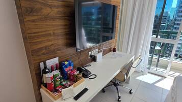 Een hotelkamer met een houten accentmuur, een flatscreen-tv, een bureau met stoel, en uitzicht op de stad door grote ramen.