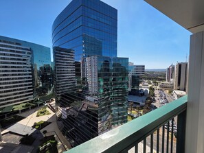 A high-rise building with a curved glass facade, surrounded by other modern buildings, and a view of a parking area below.