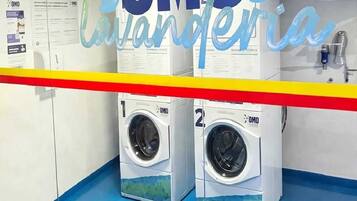 Une buanderie équipée de deux machines à laver, avec un sol bleu et une barrière rayée de jaune et de rouge.