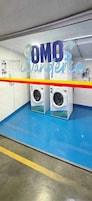 Un cuarto de lavandería con dos lavadoras, piso azul y una barrera rayada en amarillo y rojo.