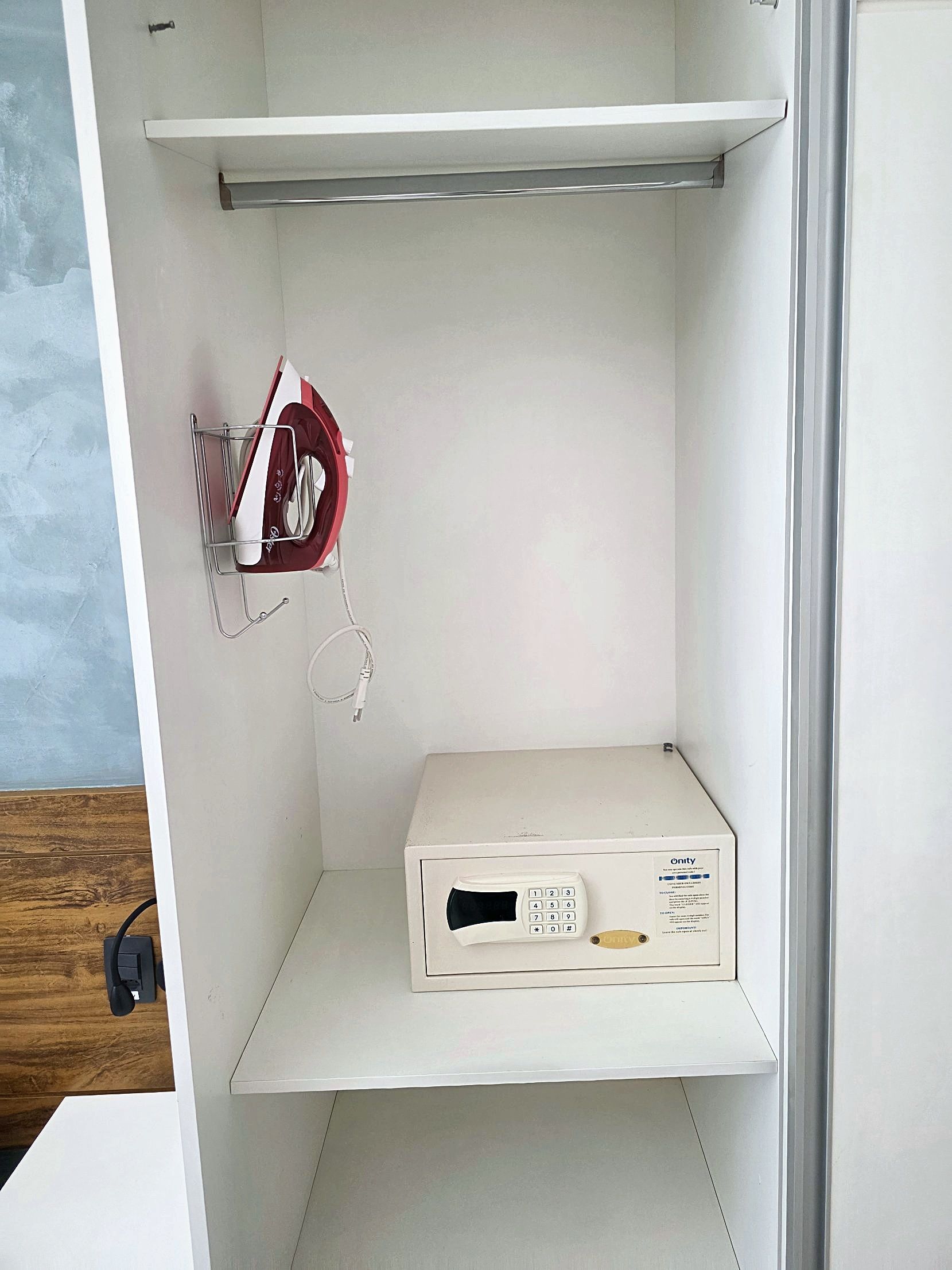 Une pièce blanche avec une étagère sur laquelle se trouvent une boîte blanche et un fer à repasser rouge et blanc.