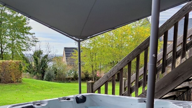 Ein Whirlpool unter einer überdachten Terrasse mit einer Holzterrasse und einer Treppe, die hinaufführt.