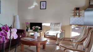 Ein Wohnzimmer mit einer Couch, einem runden Tisch, einem Sessel, einem Fernseher und einer dekorativen Vase mit Blumen.