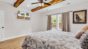 Een slaapkamer met een bed, een plafondventilator, een raam met gordijnen en een deur.