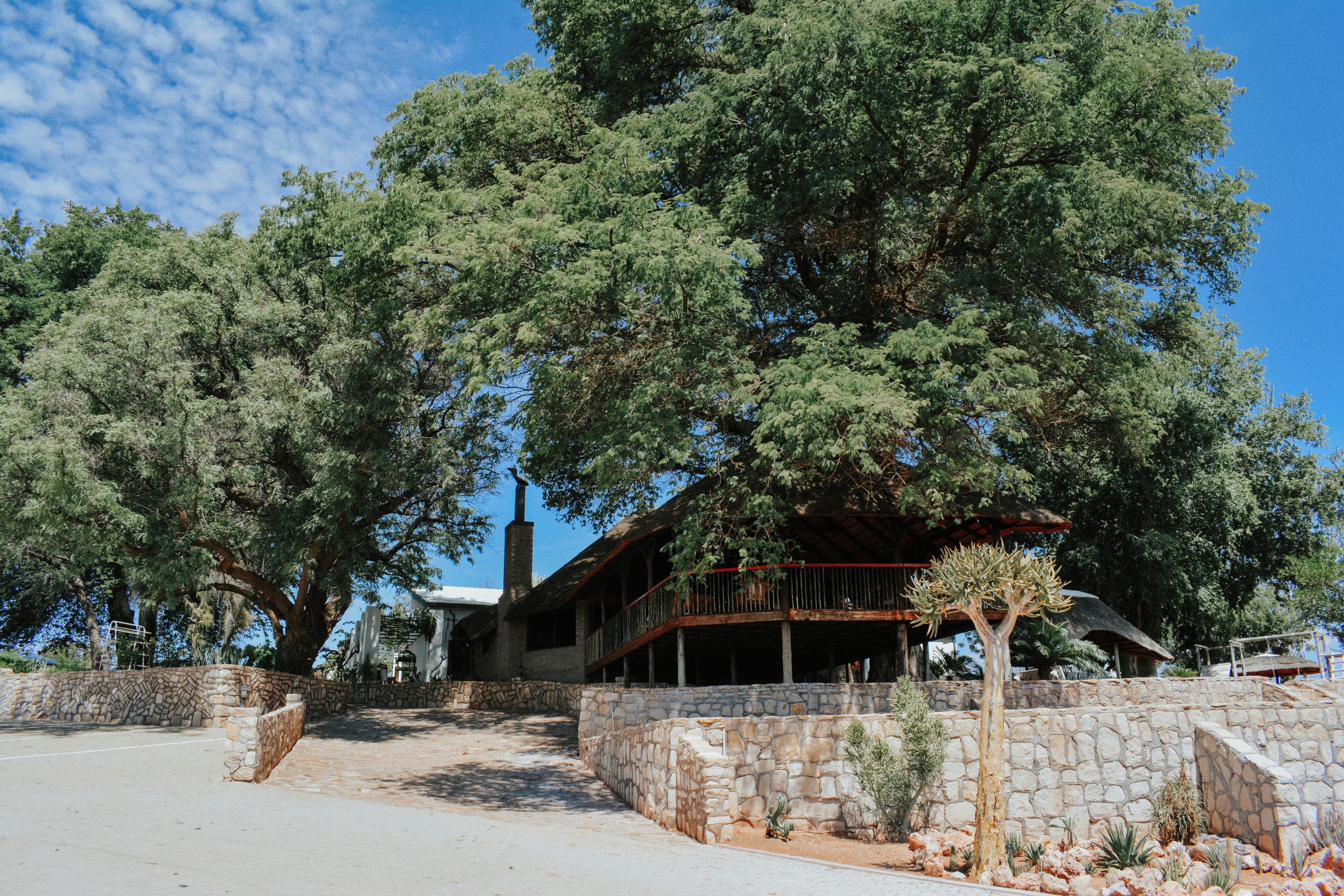 Edifício de paredes de pedra com uma varanda voltada para um pátio, rodeado por árvores.