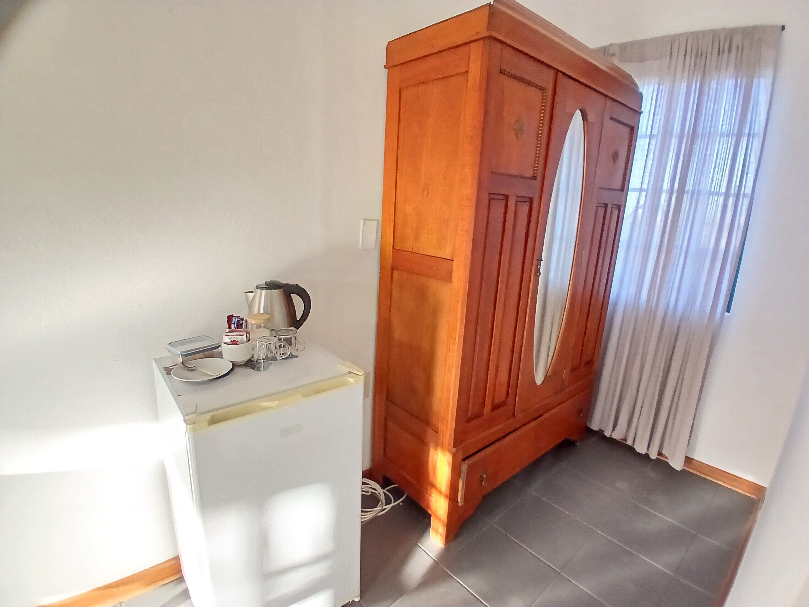 Uma pequena cozinha compacta com geladeira branca, armário de madeira e janela com cortinas.
