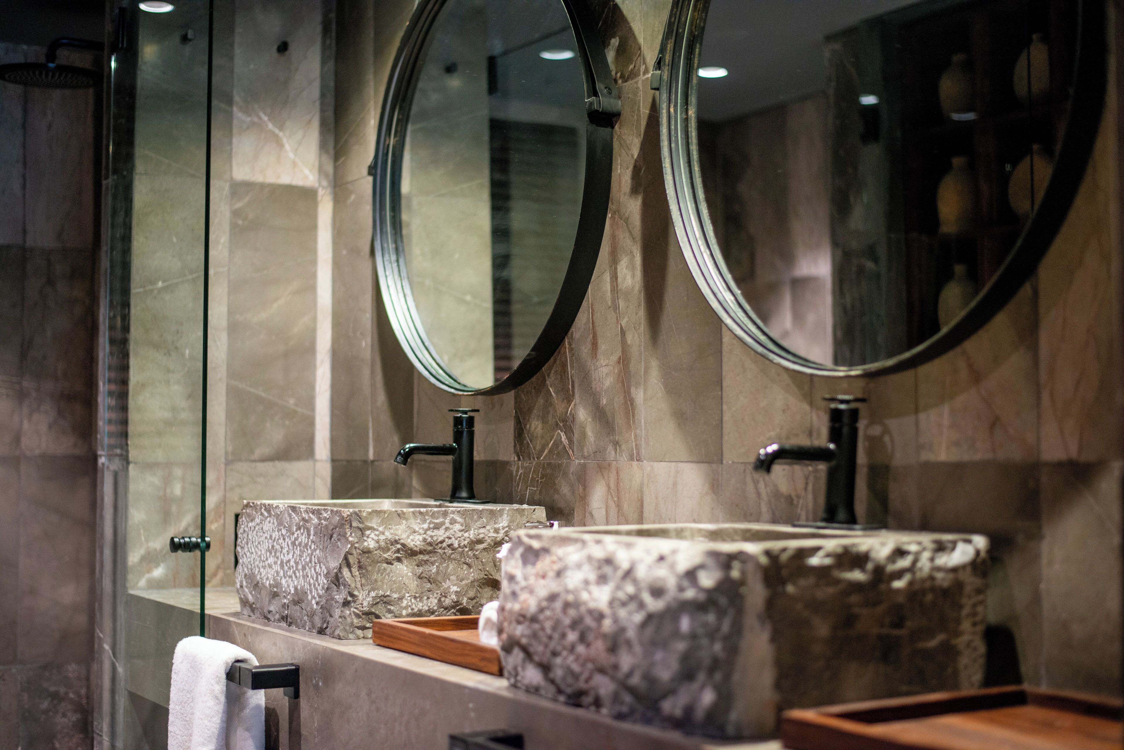 A bathroom with a large mirror, two sinks with stone-like countertops, and a towel rack.