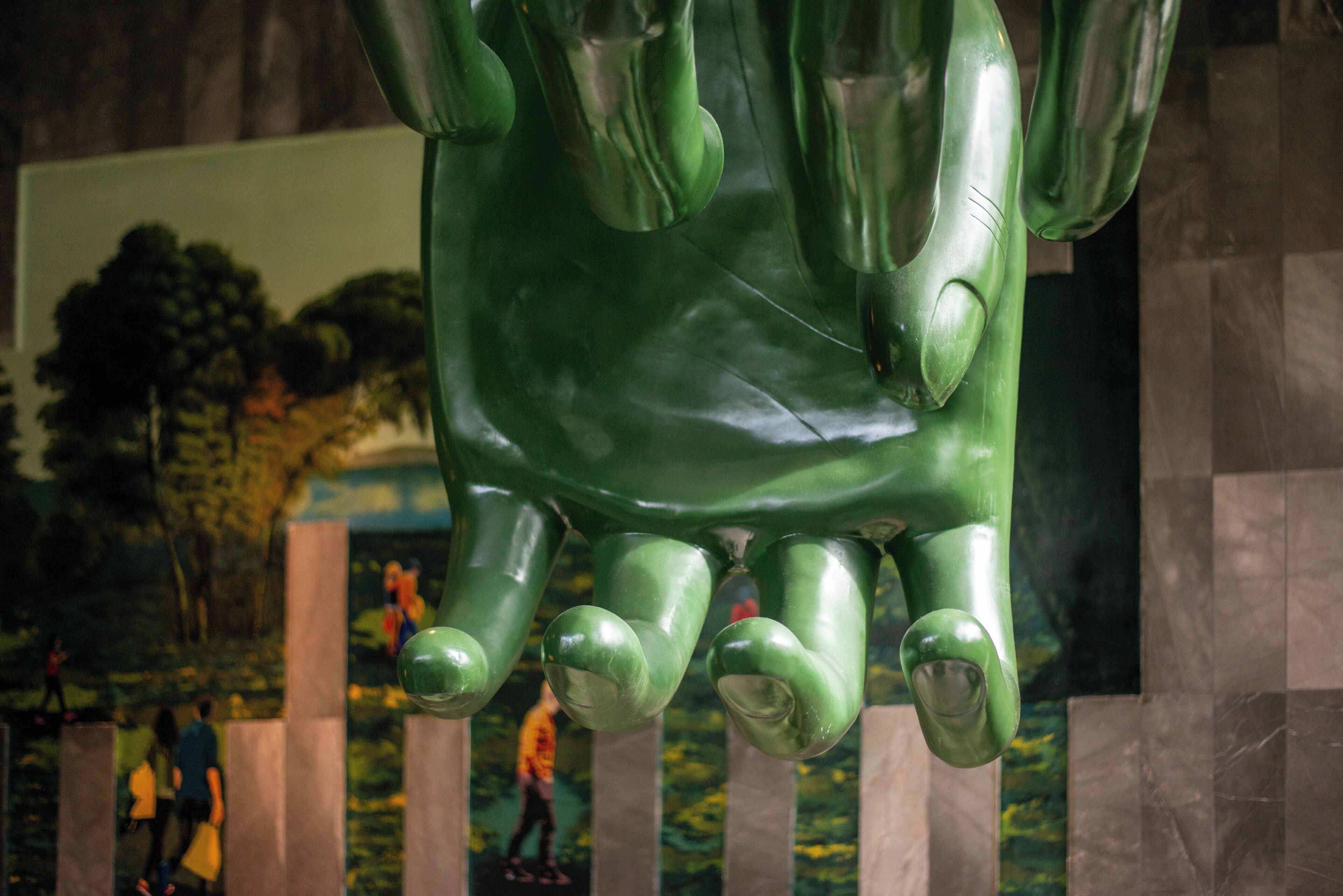 A large green sculpture with a textured surface, possibly made of metal or stone, with a reflective quality.