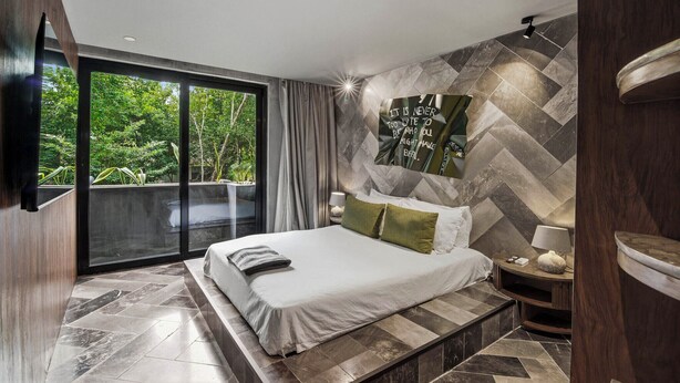 A modern bedroom with a large bed, a view of greenery through a sliding door, and a herringbone-patterned wall. - Rooftop Pool, Spa! Luxury 4BR Designer Tulum Villa (Tulum)