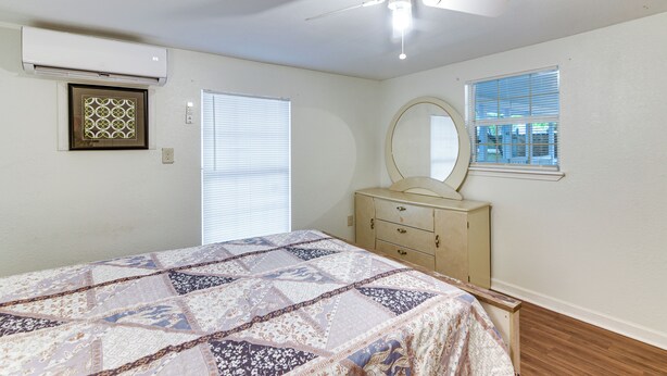 A bedroom with a bed, dresser, ceiling fan, air conditioning unit, window blinds, and a mirror. - Inviting Unit, 10 Mi to Airport & Vintage Park! (Houston)