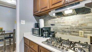 Una cocina con armarios de madera, estufa a gas, microondas, cafetera y licuadora.