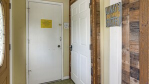 Entrada de hotel con una puerta blanca cerrada, un letrero de bienvenida, un teclado de cierre y una pared de madera con un cartel que dice 'Always Grateful'.