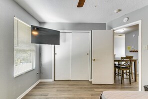 Ein Zimmer mit einem wandmontierten Flachbildfernseher, einer geschlossenen Tür, einem Essbereich mit Tisch und Stühlen sowie einem Deckenventilator.
