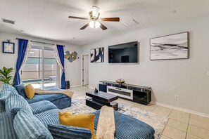A living room with a ceiling fan, a flat-screen TV, a fireplace, and a large window with curtains. - Swim, Golf & Park-hop! Family Home in Davenport (Davenport)