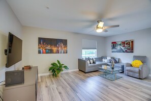 A modern living room with a flat-screen TV, a ceiling fan, a sofa, a coffee table, and artwork on the walls. - Walk to Shops & Eats! Cape Coral Extended Escape (Cape Coral)