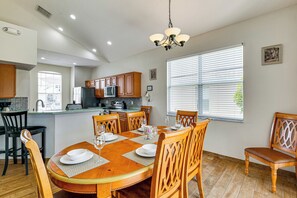 A modern kitchen with wooden cabinets, a central island, and a dining area with a round table and chairs. - Pool & Game Room! Family Home 13 Mi to Disney (Davenport)