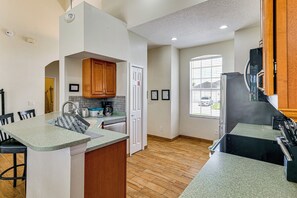 A modern kitchen with a central island, wooden cabinets, and a view of the outside through a window. - Pool & Game Room! Family Home 13 Mi to Disney (Davenport)