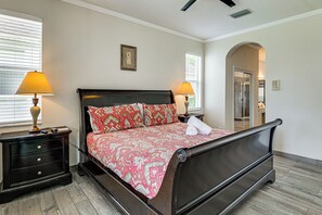 Habitación de hotel con cama, dos mesitas de noche, una lámpara de noche, ventana con persianas, puerta y ventilador de techo.