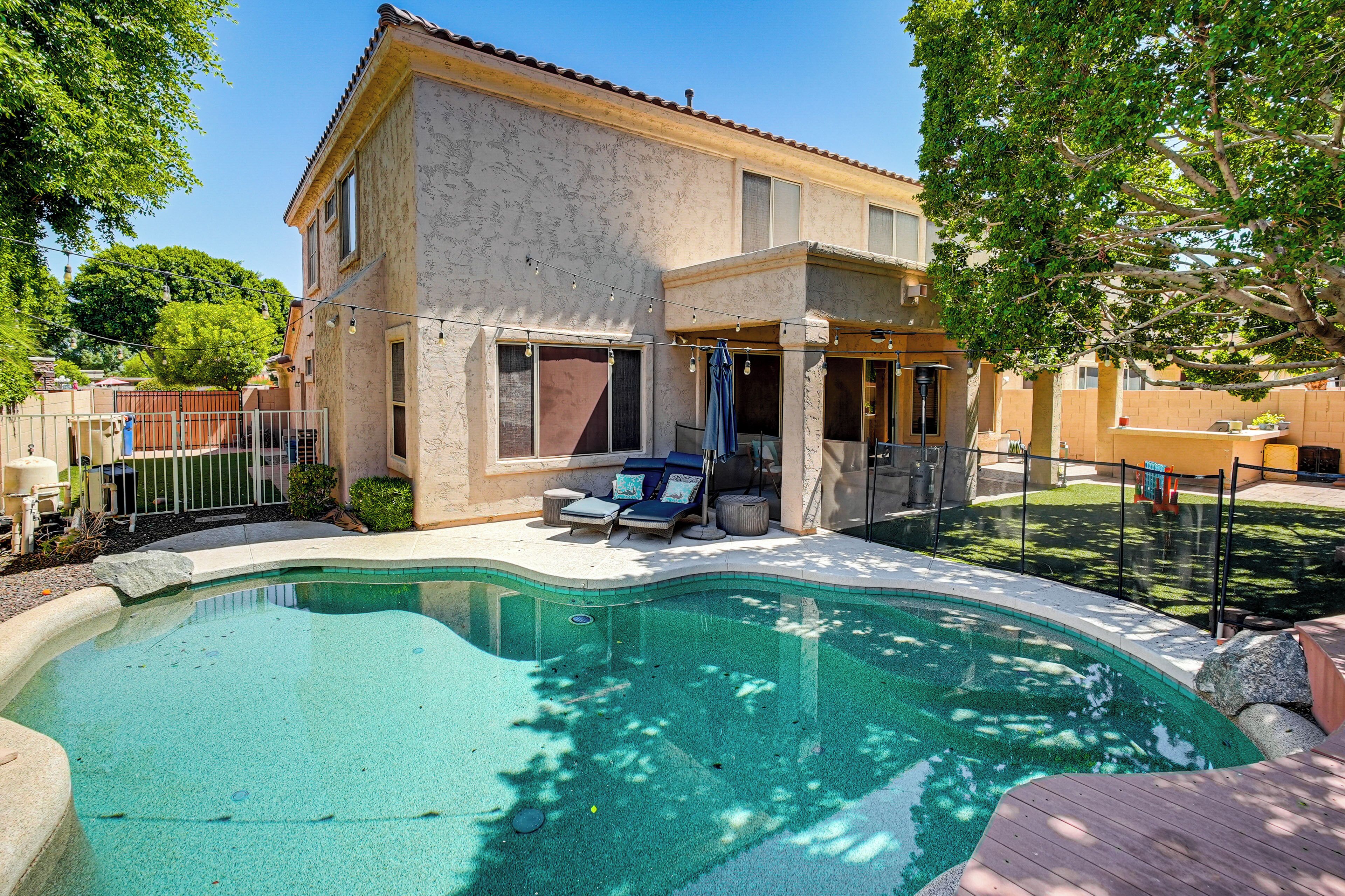 A two-story house with a swimming pool, outdoor seating, and a fenced yard.