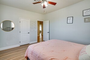 Un dormitorio con cama, ventilador de techo, una puerta y un pasillo que conduce a otra habitación.