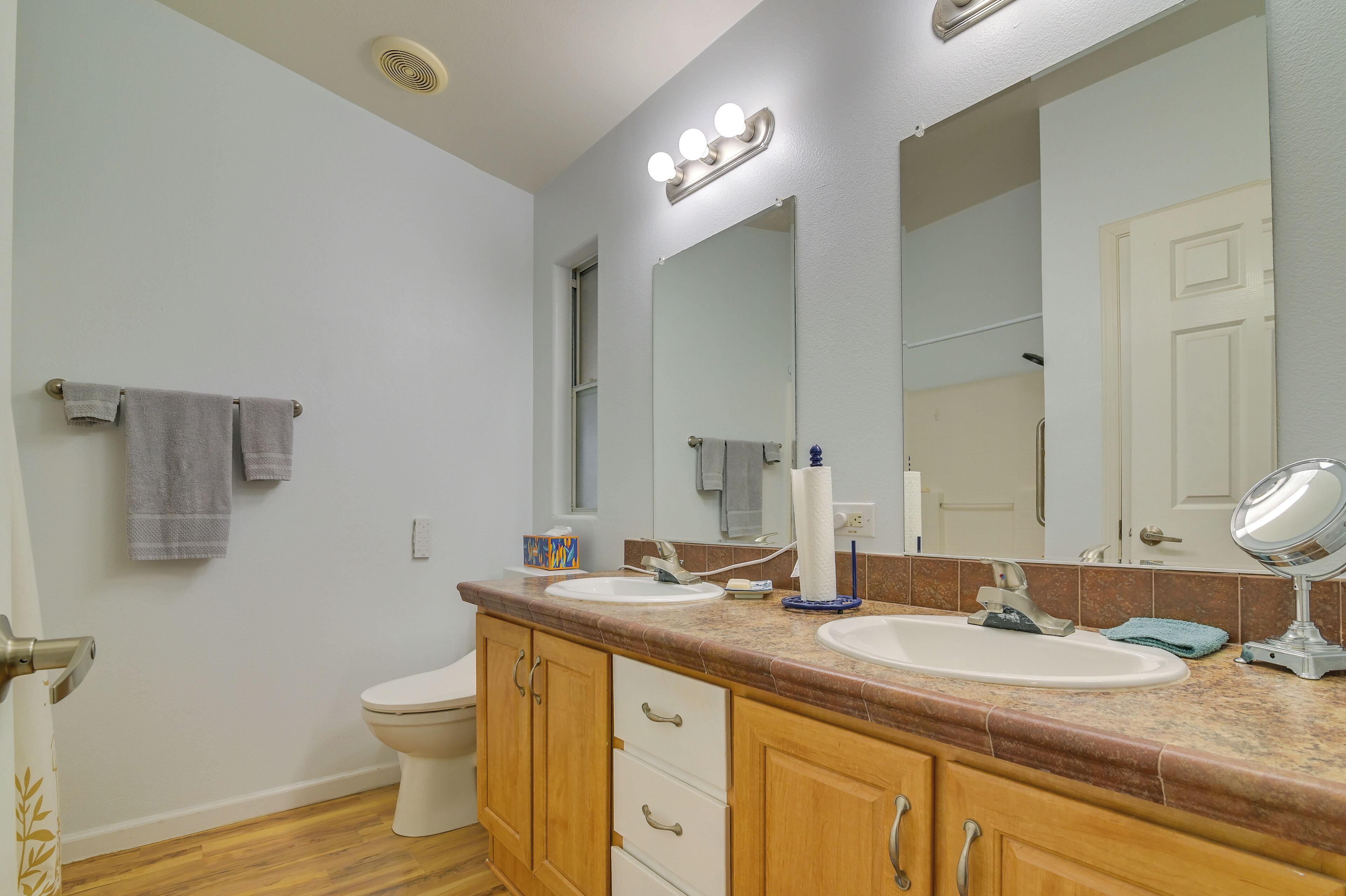 A bathroom with a double sink vanity, a toilet, a mirror with lights, and a towel rack.