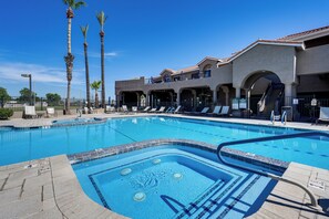 A swimming pool with lounge chairs, palm trees, and a building with arches and balconies. - Complimentary Golf Cart! Viewpoint Resort Home (Mesa)