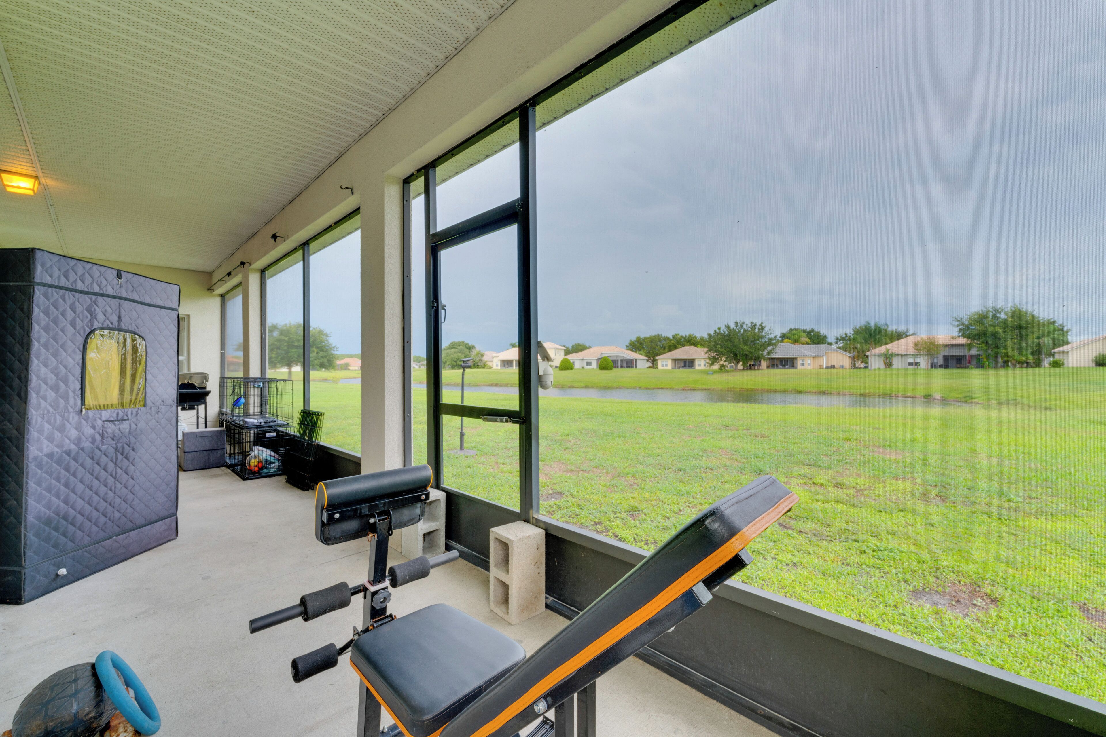 A covered outdoor area with exercise equipment, a view of a grassy field, and a building in the background.