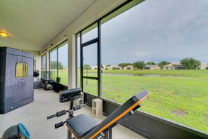 A covered outdoor area with exercise equipment, a view of a grassy field, and a building in the background.